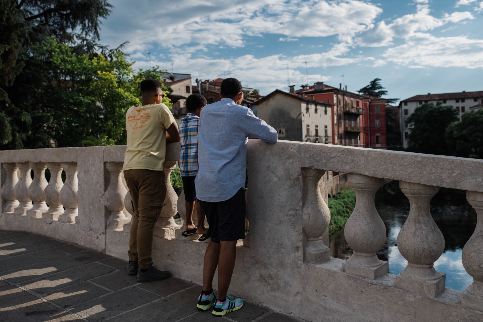 A father and two sons pausing together on a bridge overlooking the water and an Italian town.